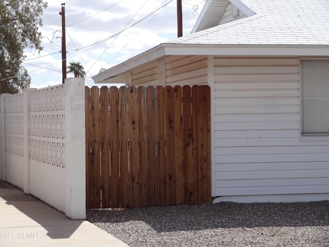 view of side of home with a shingled roof, a gate, and fence