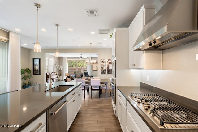 kitchen with visible vents, dark countertops, appliances with stainless steel finishes, wall chimney range hood, and a sink