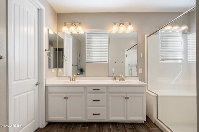 full bath featuring double vanity, wood finish floors, a sink, and a stall shower