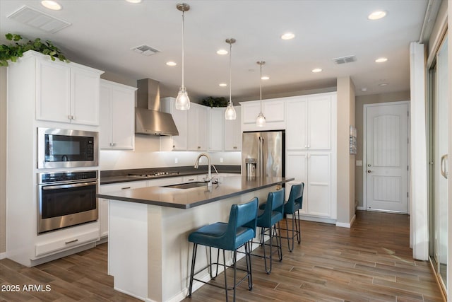 kitchen featuring wall chimney range hood, visible vents, appliances with stainless steel finishes, and a sink