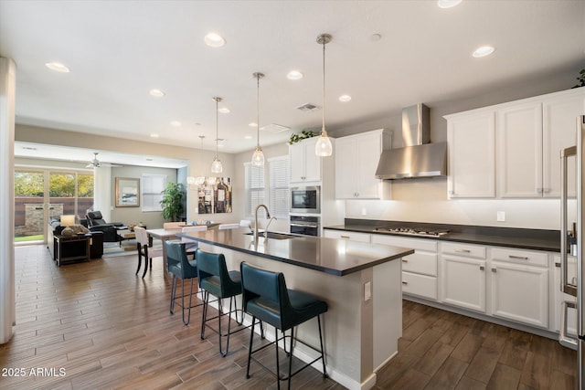 kitchen with stainless steel appliances, dark countertops, a sink, and wall chimney exhaust hood