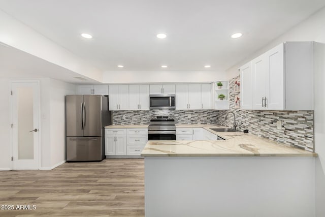 kitchen with light wood finished floors, open shelves, appliances with stainless steel finishes, a sink, and a peninsula