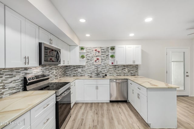 kitchen featuring white cabinets, a peninsula, stainless steel appliances, open shelves, and a sink