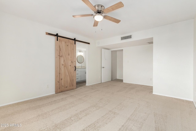 spare room featuring ceiling fan, a barn door, light colored carpet, visible vents, and baseboards