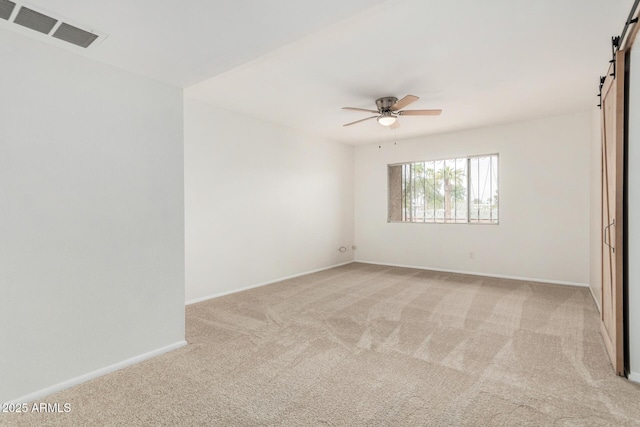 empty room with a barn door, light carpet, visible vents, baseboards, and a ceiling fan