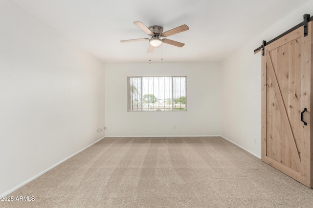 unfurnished bedroom featuring light colored carpet, ceiling fan, baseboards, and a barn door