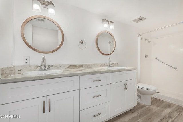 bathroom featuring double vanity, visible vents, toilet, a sink, and wood finished floors