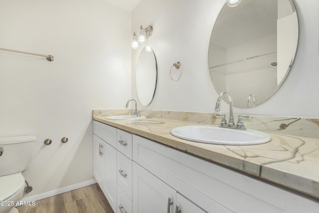 full bath with double vanity, a sink, toilet, and wood finished floors