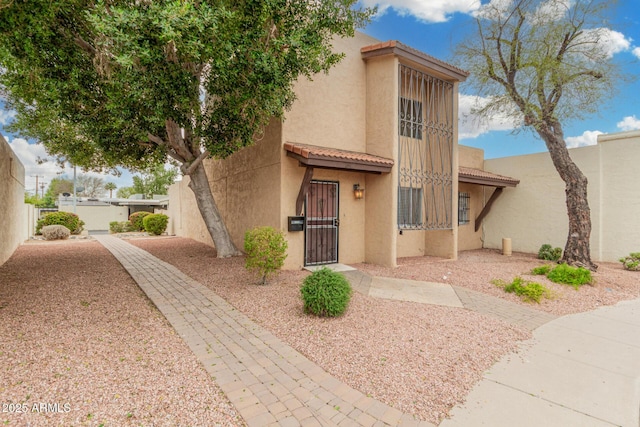 pueblo-style house featuring a tiled roof, fence, and stucco siding