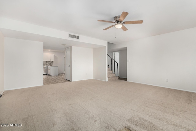 unfurnished room featuring light carpet, visible vents, baseboards, ceiling fan, and stairs