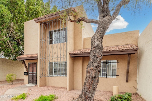 rear view of property with a tile roof, fence, and stucco siding