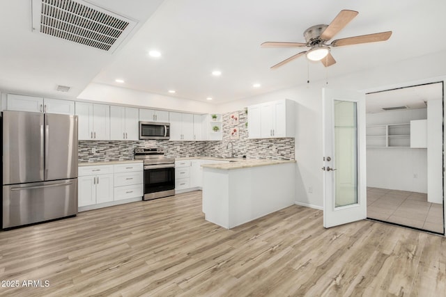 kitchen featuring light wood finished floors, light countertops, visible vents, appliances with stainless steel finishes, and a peninsula