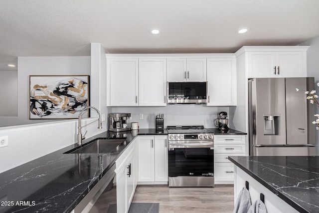 kitchen featuring appliances with stainless steel finishes, sink, white cabinets, and dark stone counters