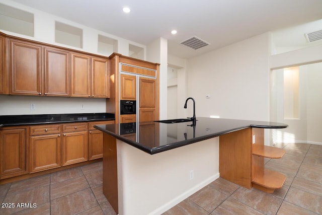 kitchen with dark countertops, visible vents, brown cabinets, and a sink