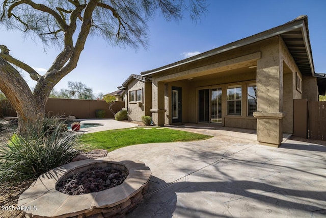 back of house with stucco siding, an outdoor fire pit, a fenced backyard, and a patio area