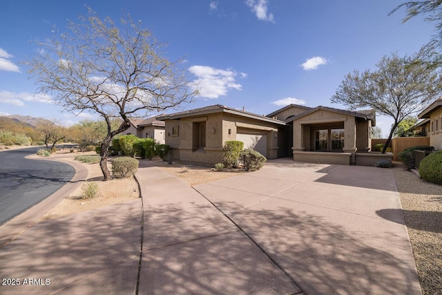 view of front of house with fence, a tiled roof, stucco siding, a garage, and driveway