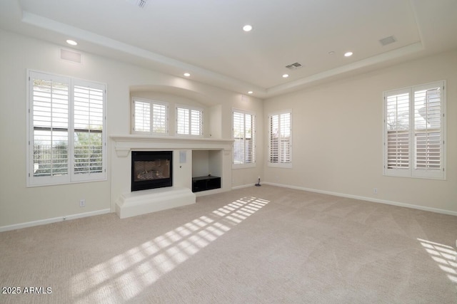 unfurnished living room featuring a tray ceiling, light colored carpet, visible vents, and a glass covered fireplace