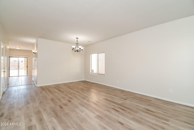 unfurnished room featuring a notable chandelier and light hardwood / wood-style flooring