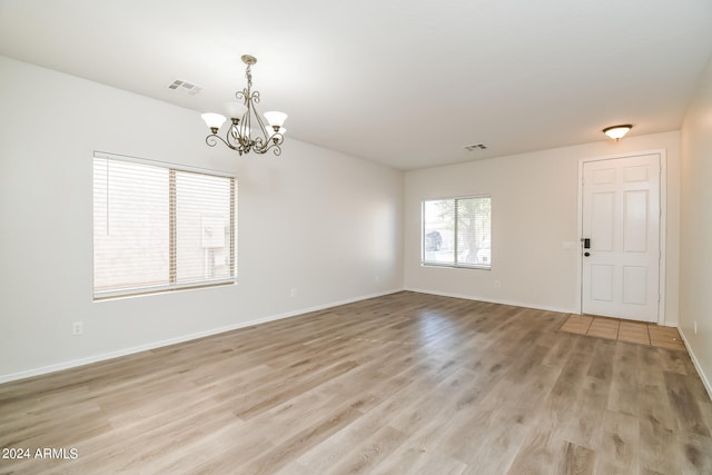 empty room featuring a notable chandelier and light wood-type flooring