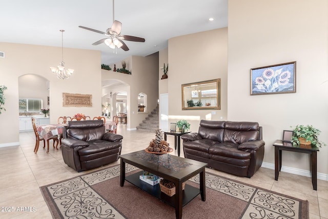 tiled living room featuring a high ceiling and ceiling fan with notable chandelier