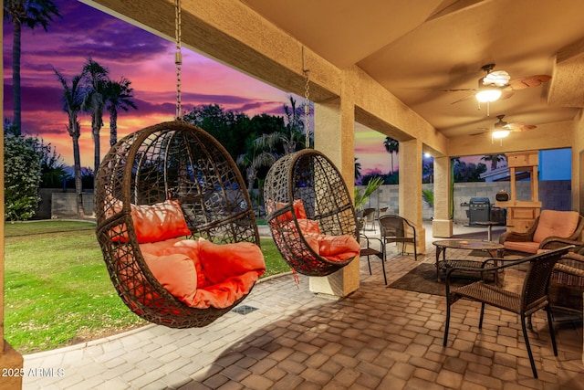 patio terrace at dusk featuring a lawn, outdoor lounge area, and ceiling fan