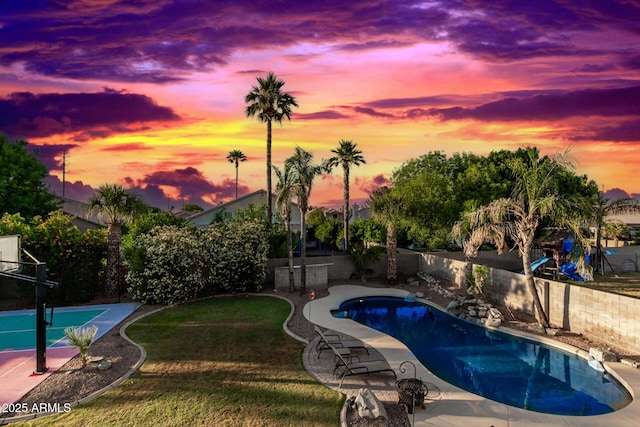 pool at dusk with basketball hoop and a lawn