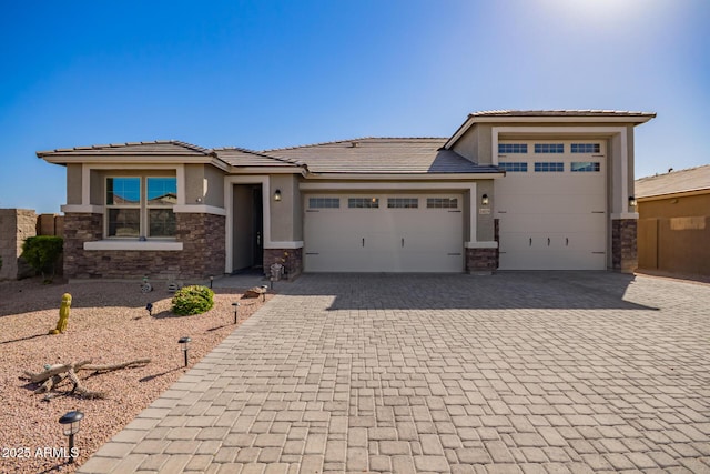 prairie-style home with a tile roof, stucco siding, decorative driveway, stone siding, and an attached garage