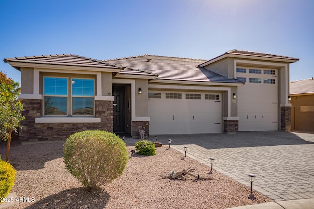 prairie-style home with decorative driveway, stone siding, an attached garage, and stucco siding