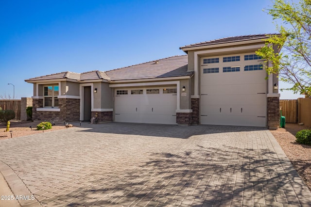 prairie-style home with fence, an attached garage, stucco siding, stone siding, and decorative driveway