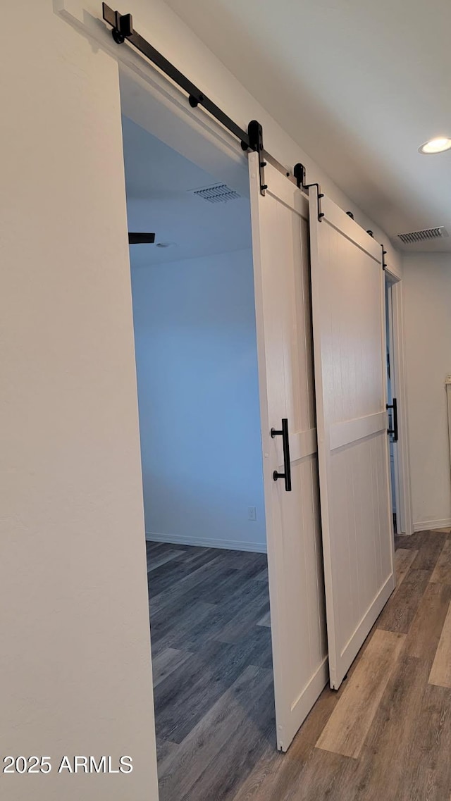 hallway featuring a barn door, wood finished floors, and baseboards