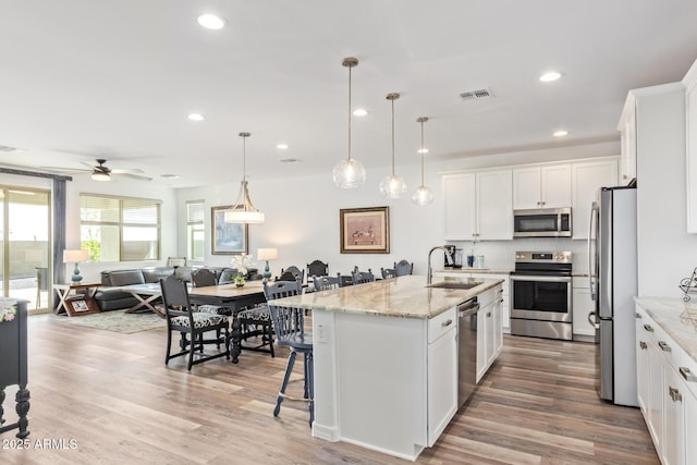 kitchen with visible vents, open floor plan, a kitchen breakfast bar, stainless steel appliances, and a sink