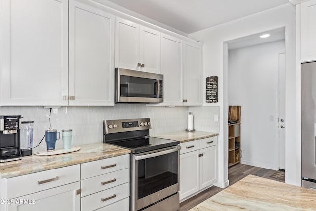 kitchen with light stone counters, wood finished floors, stainless steel appliances, white cabinetry, and backsplash