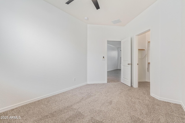 unfurnished bedroom with light carpet, a walk in closet, a closet, and ceiling fan