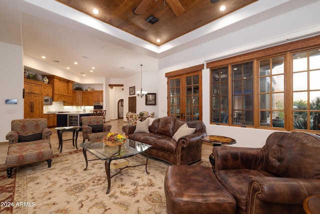 living room with ceiling fan with notable chandelier, wooden ceiling, and a tray ceiling