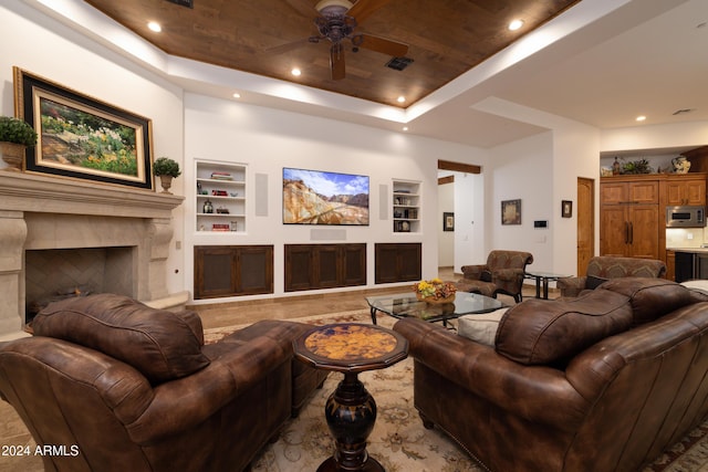 living room featuring ceiling fan, a raised ceiling, built in features, and a premium fireplace