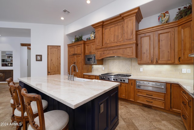 kitchen with decorative backsplash, stainless steel appliances, a kitchen island with sink, sink, and a breakfast bar area