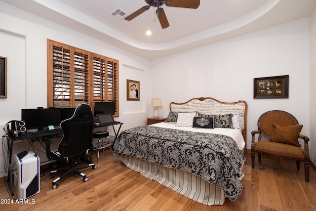 bedroom featuring ceiling fan, a raised ceiling, and wood-type flooring