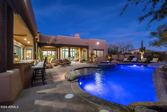 pool at dusk featuring an outdoor hangout area, an outdoor bar, ceiling fan, an in ground hot tub, and a patio area