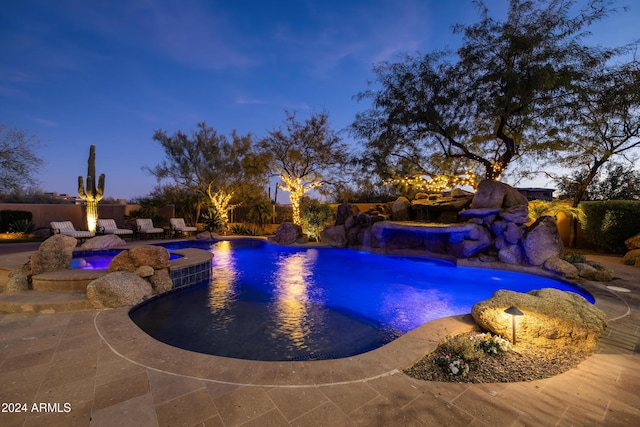 pool at dusk featuring pool water feature, a patio area, and a jacuzzi