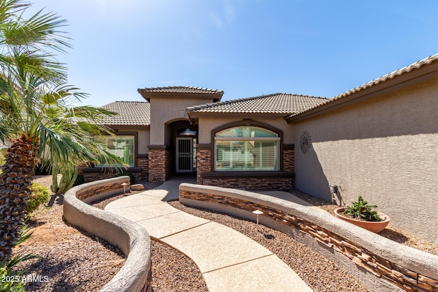 view of exterior entry with stone siding, a tiled roof, and stucco siding