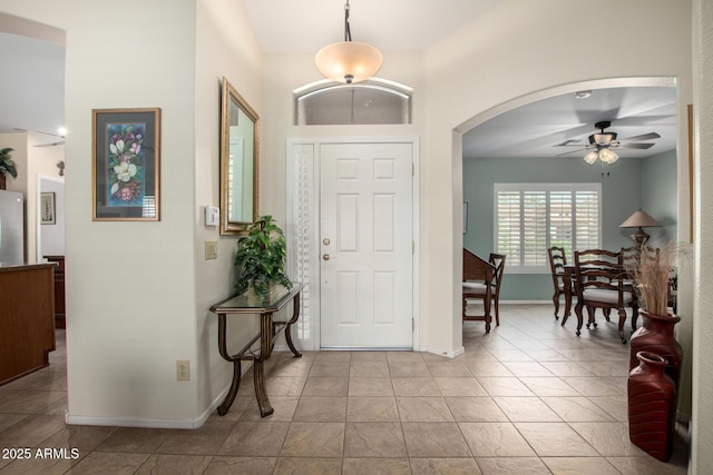 foyer with baseboards, arched walkways, a ceiling fan, and light tile patterned flooring