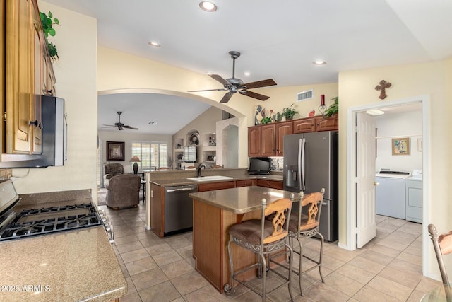 kitchen featuring arched walkways, a sink, washer and dryer, open floor plan, and appliances with stainless steel finishes