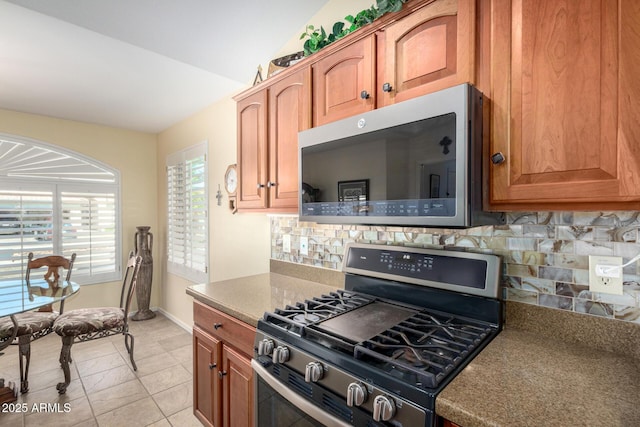 kitchen with baseboards, decorative backsplash, appliances with stainless steel finishes, vaulted ceiling, and light tile patterned flooring