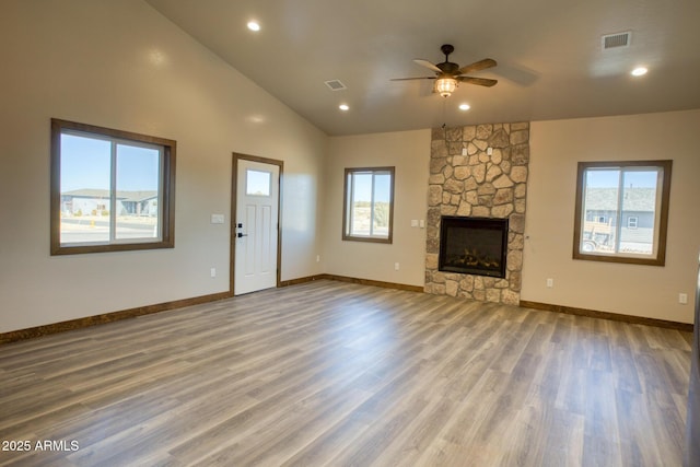 unfurnished living room featuring baseboards, visible vents, wood finished floors, and a stone fireplace