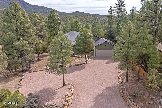 view of front of house with dirt driveway, fence, a forest view, a mountain view, and a garage