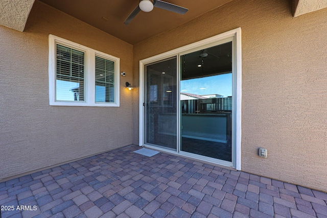 view of exterior entry featuring a patio, a ceiling fan, and stucco siding