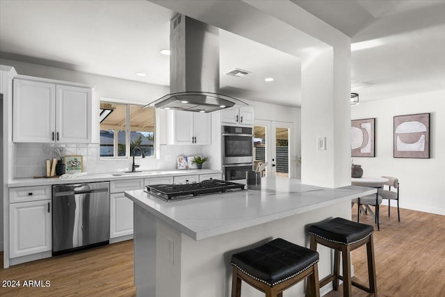 kitchen with white cabinetry, sink, light hardwood / wood-style flooring, island range hood, and appliances with stainless steel finishes