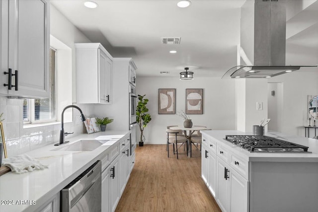 kitchen with island exhaust hood, stainless steel appliances, sink, light hardwood / wood-style flooring, and white cabinetry