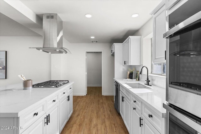 kitchen featuring light stone countertops, light hardwood / wood-style floors, island range hood, white cabinets, and appliances with stainless steel finishes