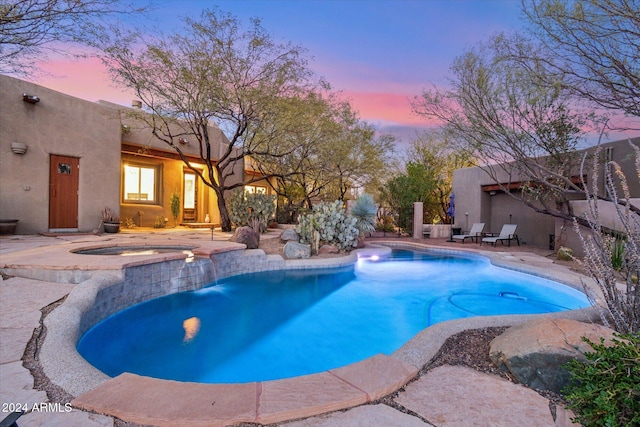 pool at dusk featuring an in ground hot tub and a patio